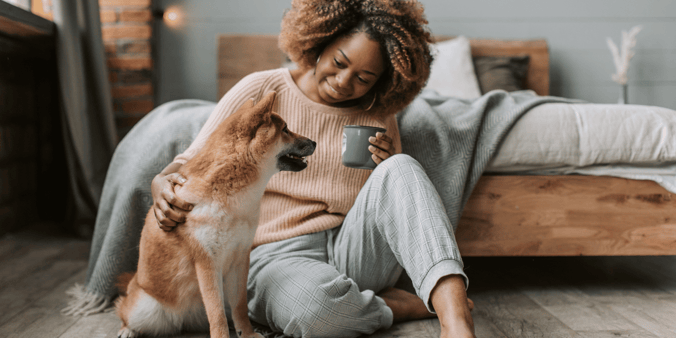 Black woman sitting on floor of bedroom with pup, smiling at each other