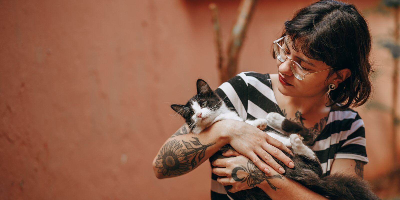 Brown-haired woman with tattoos holding a black and white cat
