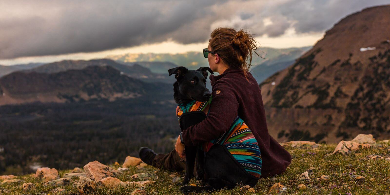 Women with arm around black lab looking into the mountains